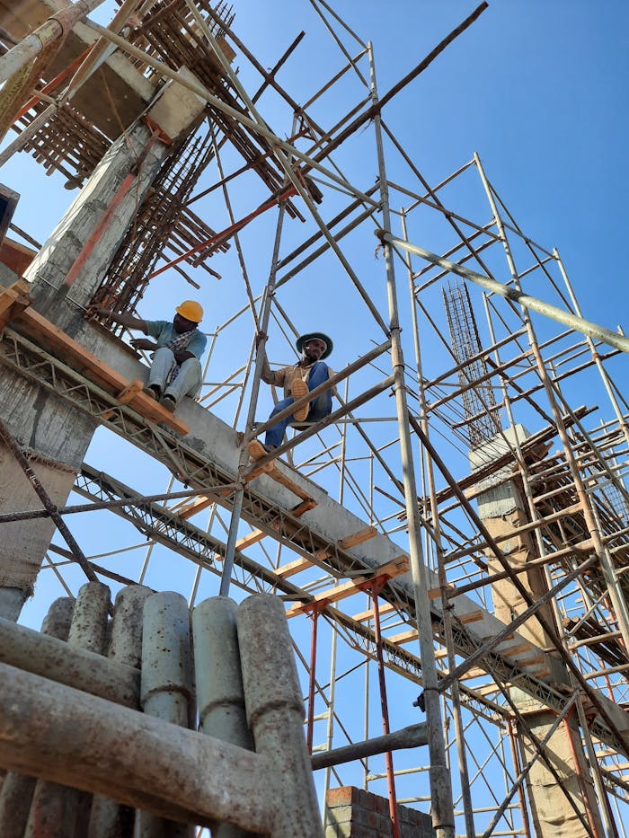 Construction workers on scaffolding at a building site under a clear sky.